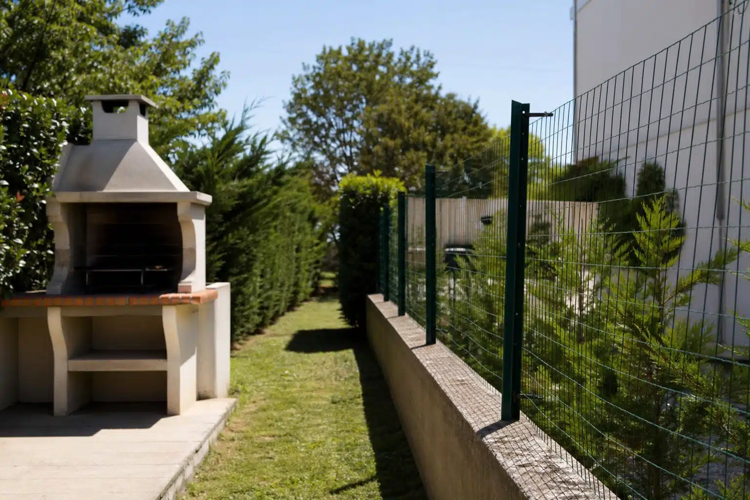 Barbecue en pierre près d'allée gazonnée et haie